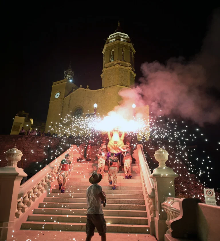 Feuergruppen und Riesen steigen die Treppe der Kirche Sant Bartomeu inmitten von Feuer und Rauch während der Baixada de les Escales in Sitges hinab.