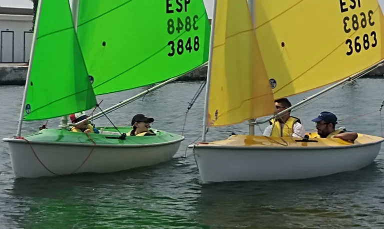 Zwei Segelboote mit Jugendlichen segeln während einer Schulregatta in Sitges auf ruhigen Gewässern.