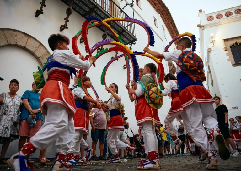 Kinder aus Sitges tanzen den Bändertanz Cintes während der Diada de Sant Tecla in bunten Trachten auf dem Dorfplatz.
