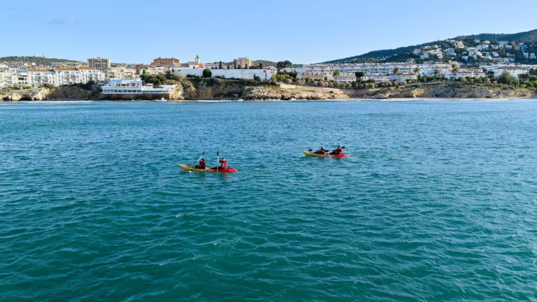 Menschen im Kajak paddeln zwischen den Buchten von Sitges mit dem Dorf im Hintergrund