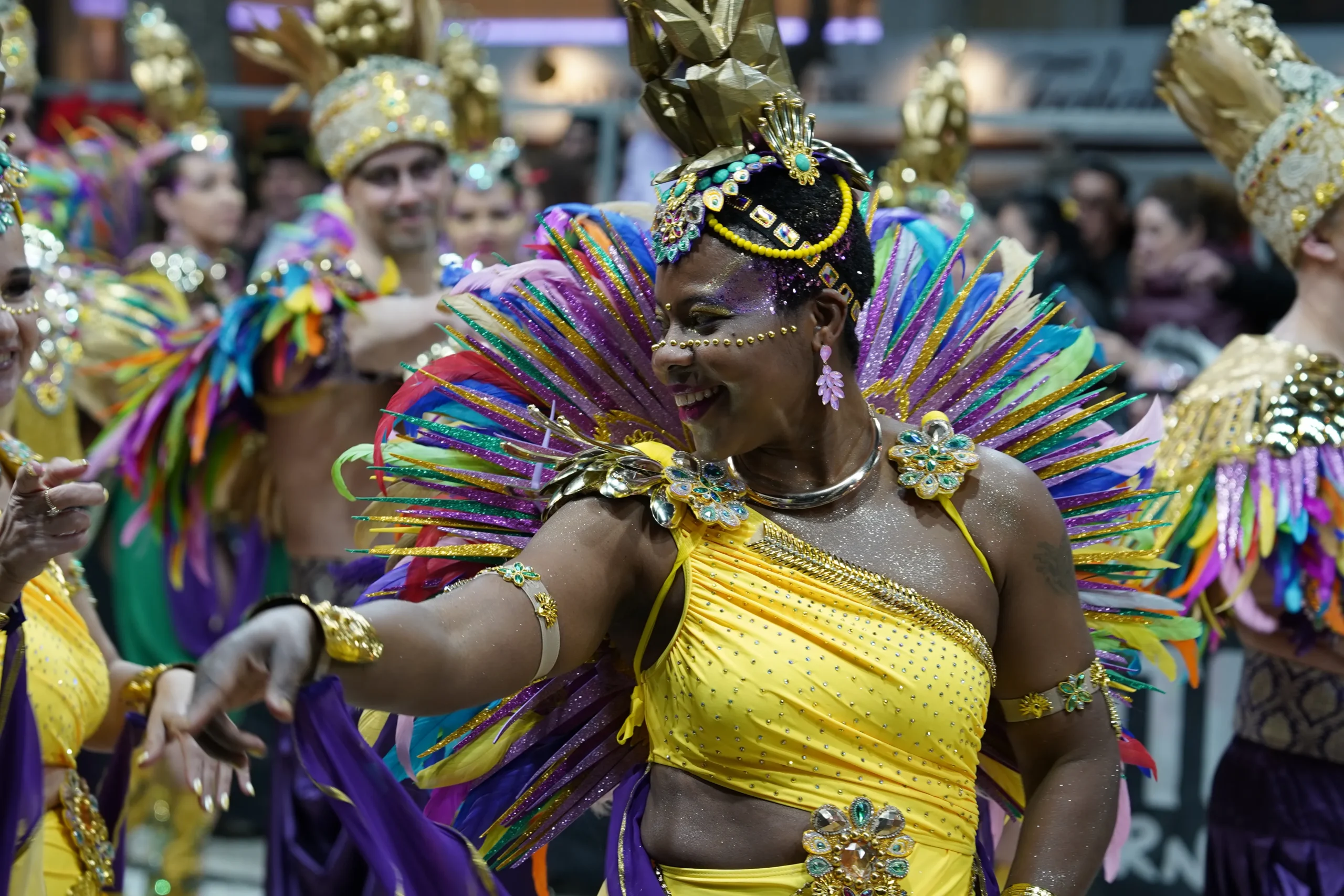 Ballarina amb tocat de plomes multicolor i vestit daurat i groc desfilant durant el Carnaval de Sitges.
